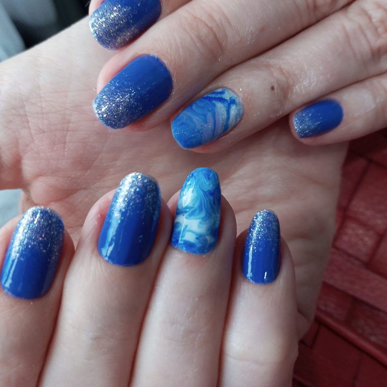 Unhas na cor azul com anelar marmorizado em branco com azul